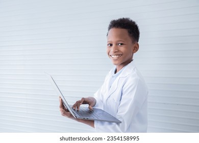 Cheerful African American boy student kid primary school hold modern technology laptop for studying in science class, cute primary school pupils happy looking at camera wearing lab coat uniform - Shutterstock ID 2354158995