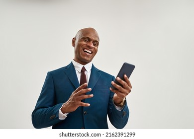 Cheerful african american businessman watching smartphone. Bald adult man wearing suit. Concept of modern successful male lifestyle. Isolated on white background. Studio shoot. Copy space - Shutterstock ID 2162391299