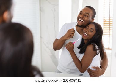 Cheerful African American Couple Having Fun While Brushing Teeth In Bathroom Together, Romantic Young African American Spouses Singing With Toothbrushes And Laughing, Selective Focus On Reflection - Powered by Shutterstock