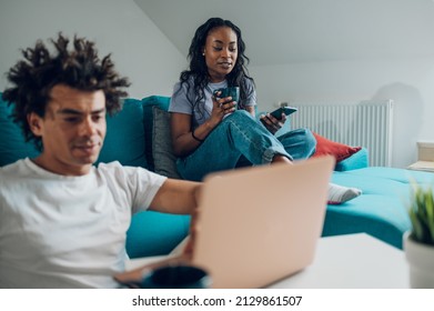 Cheerful African American Couple Spending Time In The Living Room On The Couch And Looking At Laptop Screen And Drinking Coffee While Enjoying Weekend Together.