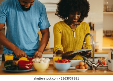 A cheerful african american couple is washing plates, and kitchen utensils, and cooking and chopping vegetables for vegan dinner at home in a kitchen. A young married couple is doing chores at home. - Powered by Shutterstock