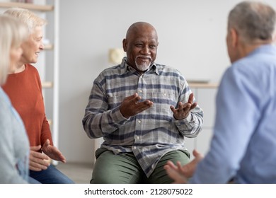 Cheerful african american elderly man having conversation with male coach while attending group therapy session with multiracial group of seniors, psychological support at nursing home concept