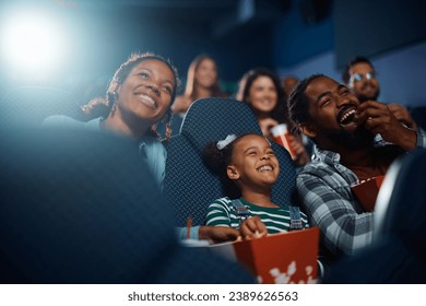 Cheerful African American family having fun while watching movie in a theater. - Powered by Shutterstock