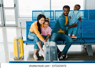 Cheerful African American Family With Travel Bags And Kids Sitting In Airport 