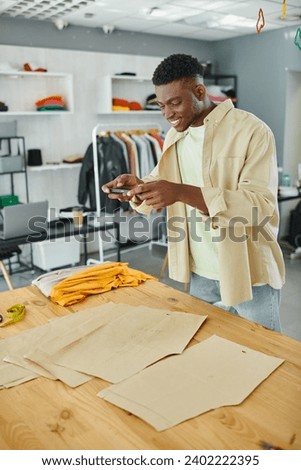 cheerful african american fashion designer taking photo of sewing patterns in own print studio