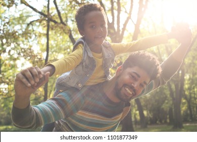 Cheerful African American Father Carrying His Daughter On Piggyback And Playing In Park.