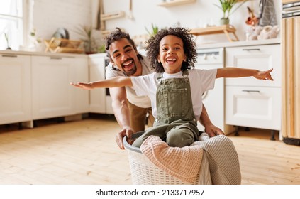 Cheerful african american father laughing and pushing basket with son  and  having fun while washing in laundry in kitchen in weekend - Powered by Shutterstock