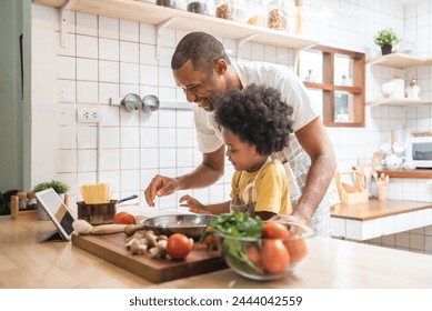 Cheerful African American Father and little child boy having video call on digital tablet with family while cooking in kitchen. Black family have fun - Powered by Shutterstock