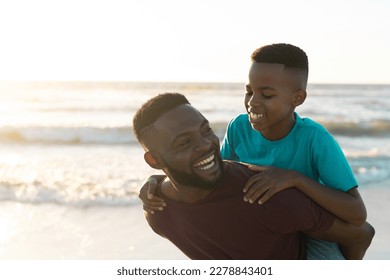 Cheerful african american father piggybacking son against beautiful seascape and clear sky at sunset. Copy space, unaltered, family, together, childhood, nature, vacation, enjoyment and summer. - Powered by Shutterstock