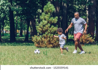cheerful african american father and son playing football in park