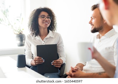 Cheerful African American female with folder smiling and talking with male coworkers during break in modern workspace - Shutterstock ID 1655440597