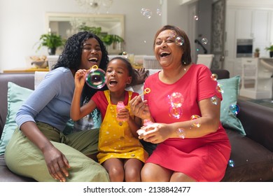 Cheerful african american girl blowing bubbles with mother and grandmother at home. unaltered, lifestyle, family, childhood, enjoyment, togetherness and leisure concept. - Powered by Shutterstock