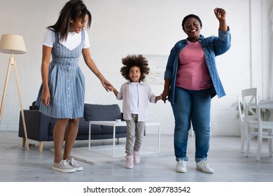 Cheerful African American Girl Holding Hands With Mother And Granny While Dancing Together In Living Room