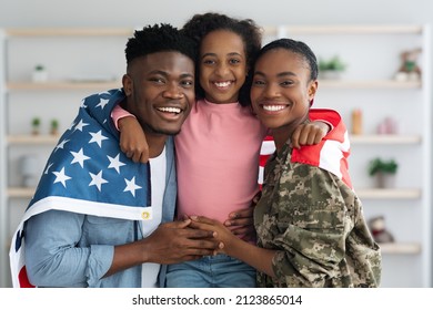 Cheerful African American Girl Teenager With Flag Of US Hugging Her Happy Parents, Patriotic Family Greeting Mother Back Home From Military Service, Embracing And Smiling, Family Portrait