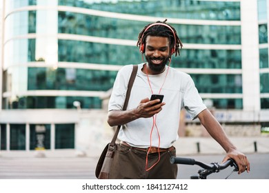 Cheerful african american guy in headphones using cellphone while standing with bicycle at city street - Powered by Shutterstock