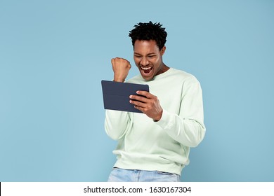 Cheerful African American Guy Holding Digital Tablet , making happy face, Standing On blue pastel Background. Studio Shot.