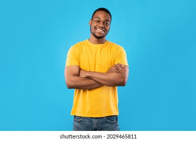 Cheerful African American Guy Smiling To Camera Posing Crossing Hands Standing Over Blue Background. Studio Shot Of Happy Self-Confident Black Millennial Man Expressing Positive Emotions