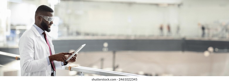 Cheerful african american guy in workwear and protective glasses medical scientist using digital tablet, analyzing data, posing at workplace, panorama with copy space. Jobs and occupations concept - Powered by Shutterstock