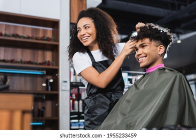Cheerful african american hairstylist and client looking away in salon