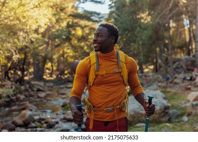 A cheerful African American hiker is standing next to a mountain stream in the forest - Powered by Shutterstock