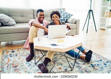Cheerful African American hipster couple watch online movies on laptop computer resting in living room together, young marriage making video Facetime call via application on netbook at cozy apartment
