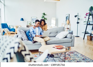 Cheerful African American Hipster Girl Making Shopping With Her Boyfriend Via Laptop Computer Spending Time At Apartment, Positive Couple In Love Watching Video On Netbook Resting In Living Room
