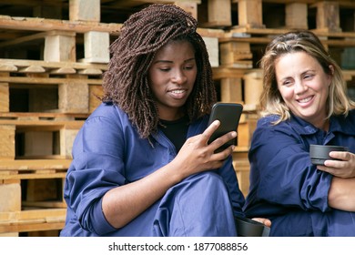 Cheerful African American industrial worker using cell during coffee break. Factory colleagues chatting while drinking coffee in warehouse. Labor or communication concept - Powered by Shutterstock