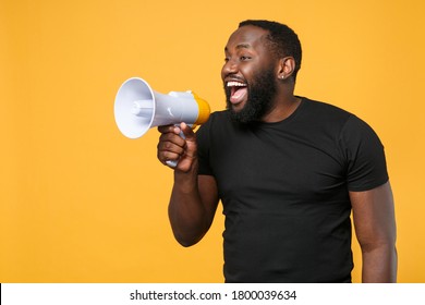 Cheerful african american man in casual black t-shirt isolated on yellow background studio portrait. People sincere emotions lifestyle concept. Mock up copy space. Scream in megaphone, looking aside