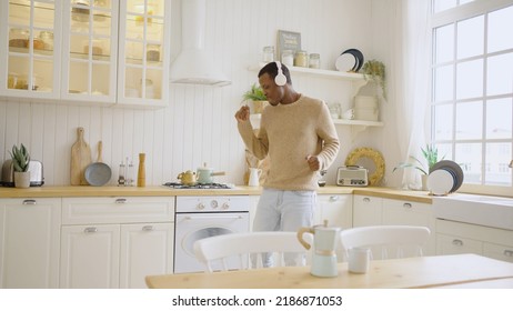 Cheerful African American man dances listening to dynamic music in headphones. Young housekeeper has fun in kitchen at home - Powered by Shutterstock