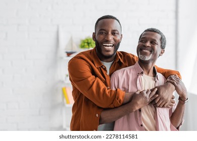 Cheerful african american man hugging mature dad and looking at camera at home