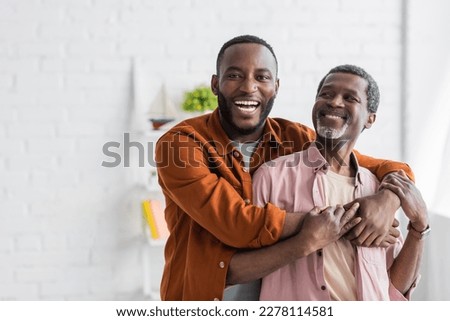 Cheerful african american man hugging mature dad and looking at camera at home