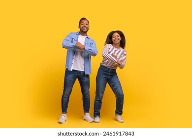 A cheerful African American man and woman stand side by side, dancing and smiling, have fun against a vivid yellow backdrop. - Powered by Shutterstock