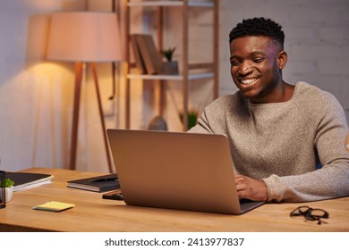 cheerful african american man working on laptop in home office at night, independent freelancer - Powered by Shutterstock