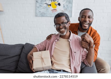 Cheerful african american middle aged man holding gift near son during father day celebration at home - Shutterstock ID 2278114519