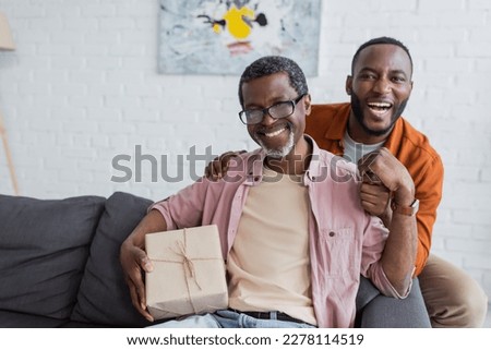 Cheerful african american middle aged man holding gift near son during father day celebration at home
