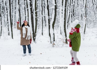 Cheerful African American Mom Smiling And Playing Snowballs With Daughter In Warm Clothing In Winter Park