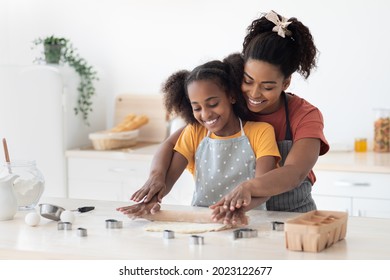 Cheerful african american mother and daughter rolling dough for homemade pastry and smiling, having fun while baking together at home, wearing aprons, kitchen interior, copy space - Powered by Shutterstock