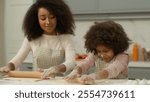 Cheerful African American mother woman teach little daughter child kid girl make flattening dough with rolling-pins in kitchen happy family use ecological products ingredients cooking together smiling