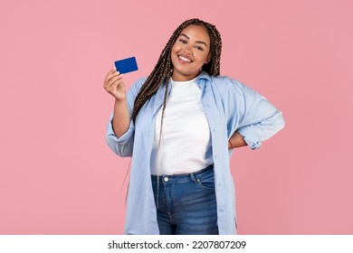 Cheerful African American Obese Woman Holding Credit Card Posing Standing Over Pink Studio Background, Smiling To Camera. Finances, Great Bank Offer Concept