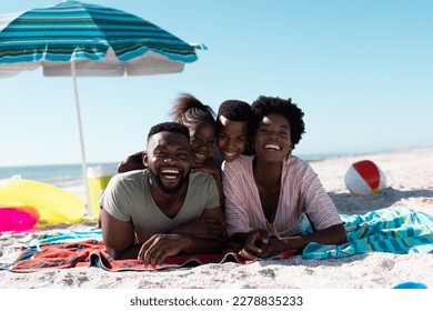 Cheerful african american parents with children lying on towels at beach under clear sky. Copy space, unaltered, family, together, parasol, picnic, nature, vacation, enjoyment, relaxing, summer. - Powered by Shutterstock