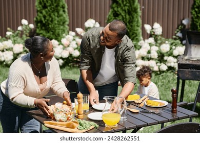 cheerful african american parents serving table in garden near son playing on backyard, family - Powered by Shutterstock