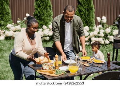 cheerful african american parents serving table in garden near son playing on backyard, shared meal - Powered by Shutterstock