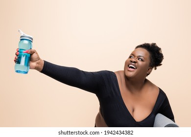 Cheerful African American Plus Size Woman In Sportswear Holding Sports Bottle Isolated On Beige