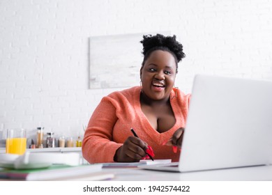 Cheerful African American Plus Size Woman Holding Pen And Looking At Laptop