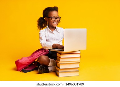 Cheerful African American Schoolgirl Sitting At Laptop Doing Homework Over Yellow Background In Studio.