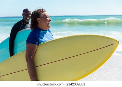 Cheerful african american senior couple carrying surfboards walking at beach on sunny day. unaltered, togetherness, active lifestyle, aquatic sport and holiday concept. - Powered by Shutterstock