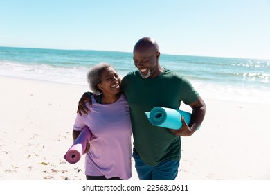 Cheerful african american senior couple with exercise mats walking against sea and clear sky. Copy space, unaltered, love, together, yoga, retirement, nature, vacation, smiling and active lifestyle. - Powered by Shutterstock