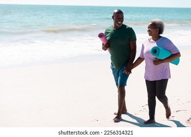 Cheerful african american senior couple with mats holding hands while walking at beach on sunny day. Unaltered, sea, love, together, yoga, retirement, nature, vacation and active lifestyle concept. - Powered by Shutterstock