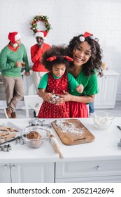 Cheerful African American Woman Embracing Daughter Preparing Christmas Cookies