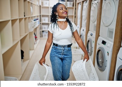 Cheerful african american woman near washing machine listening music by earphones from mobile phone in the self-service laundry. - Powered by Shutterstock